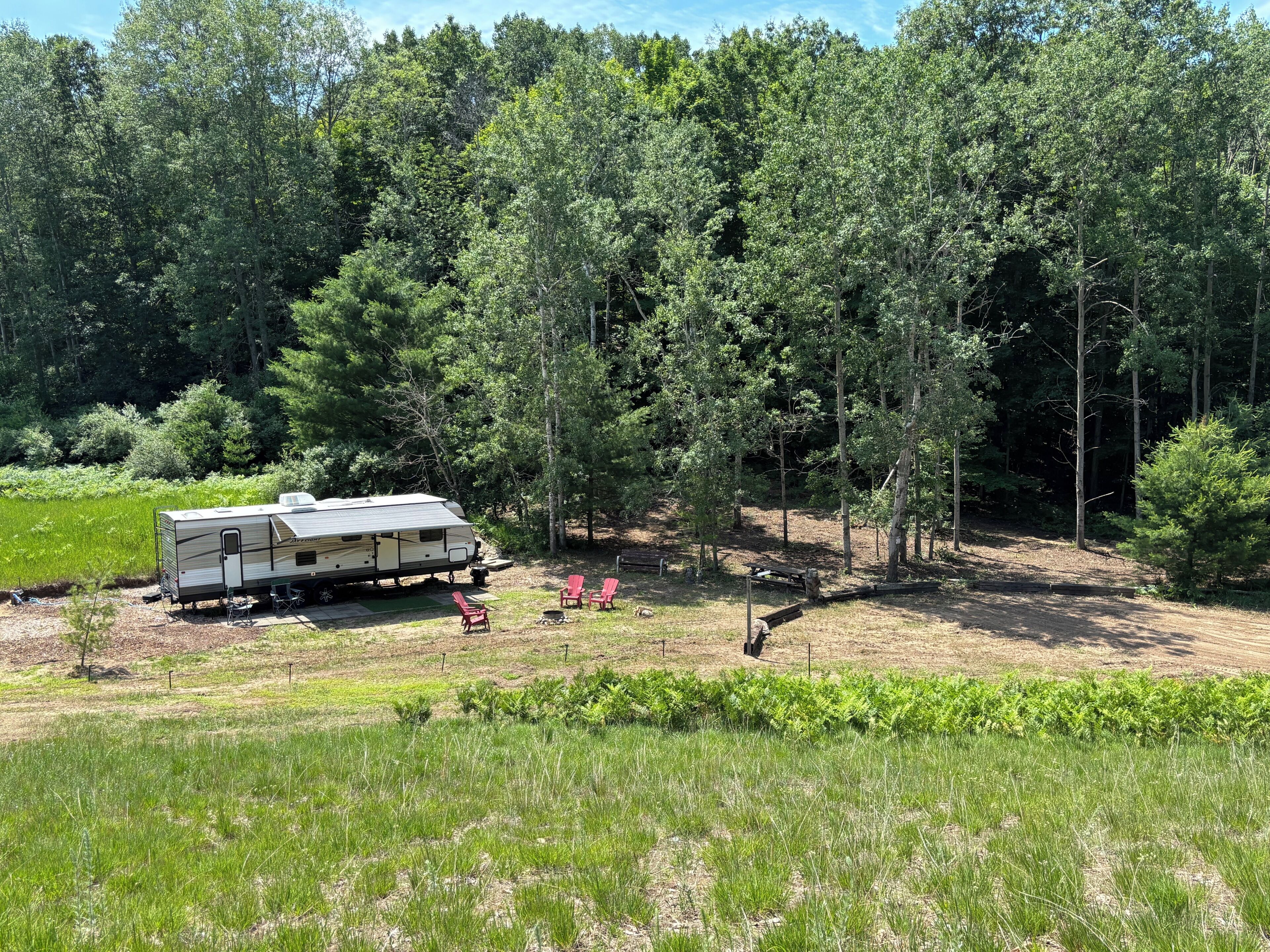 A recreational vehicle (RV) in a wooded area with a picnic table and chairs.