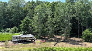 A recreational vehicle (RV) in a wooded area with a picnic table and chairs.