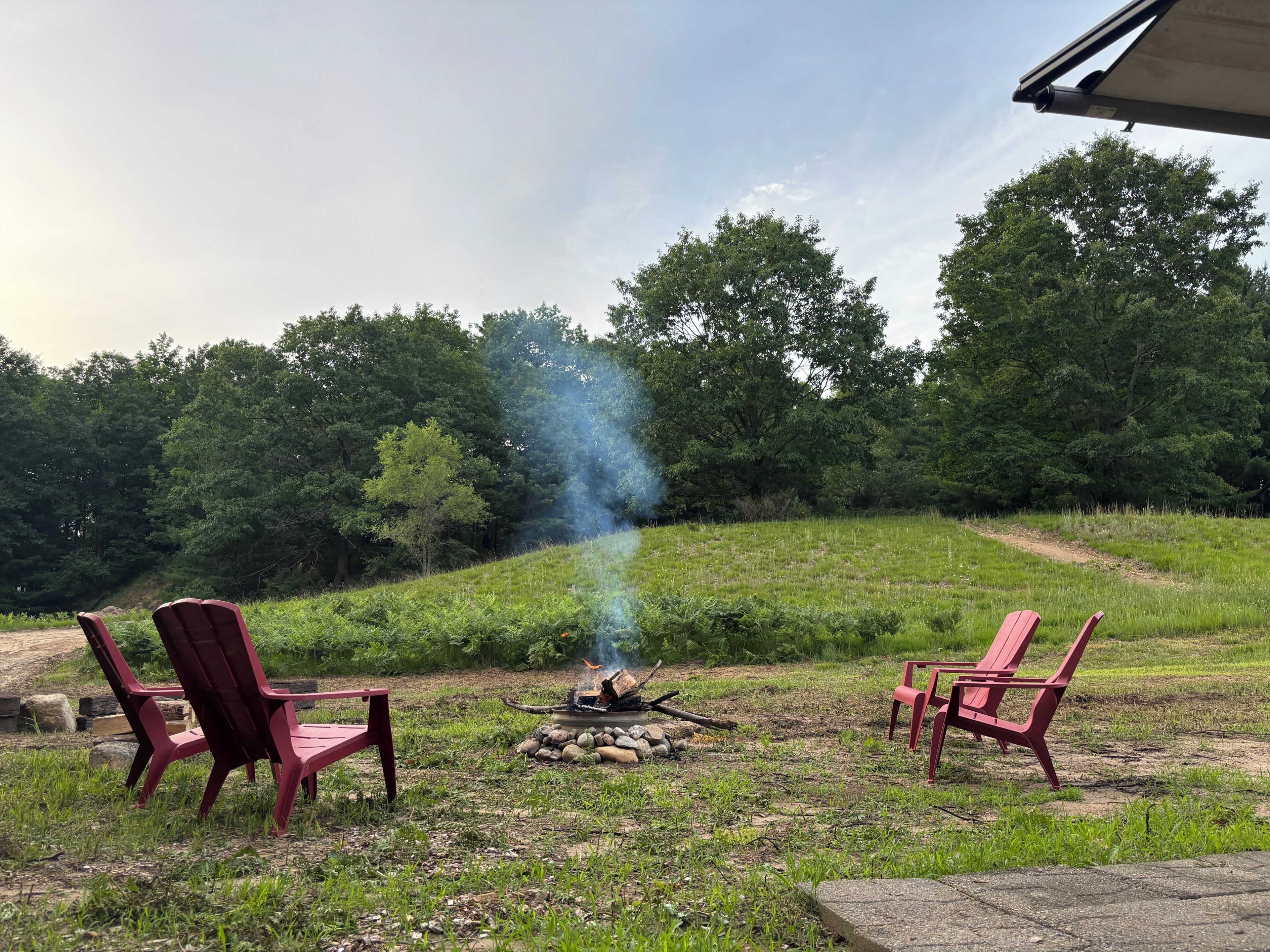 A fire pit with chairs around it, set in a grassy outdoor area with trees in the background.