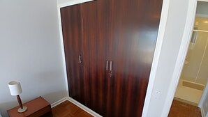 Una stanza con un armadio grande, un comodino con una lampada e un pavimento in legno.