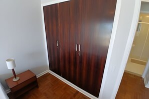 A room with a large wardrobe, a bedside table with a lamp, and a wooden floor. - SHB Frente ao Mar em Pitangueiras (Guarujá)