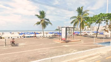 Un paseo marítimo con palmeras, una parada de autobús y sombrillas de playa.
