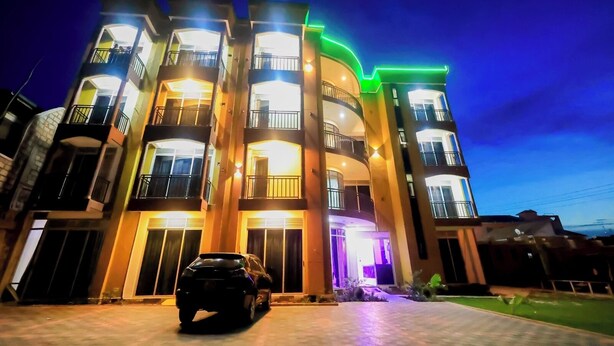 Un edificio de varios pisos con balcones, un coche estacionado adelante y una entrada bien iluminada.