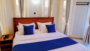 Habitación de hotel con una cama grande, una mesita de noche con teléfono y cortinas en las ventanas.