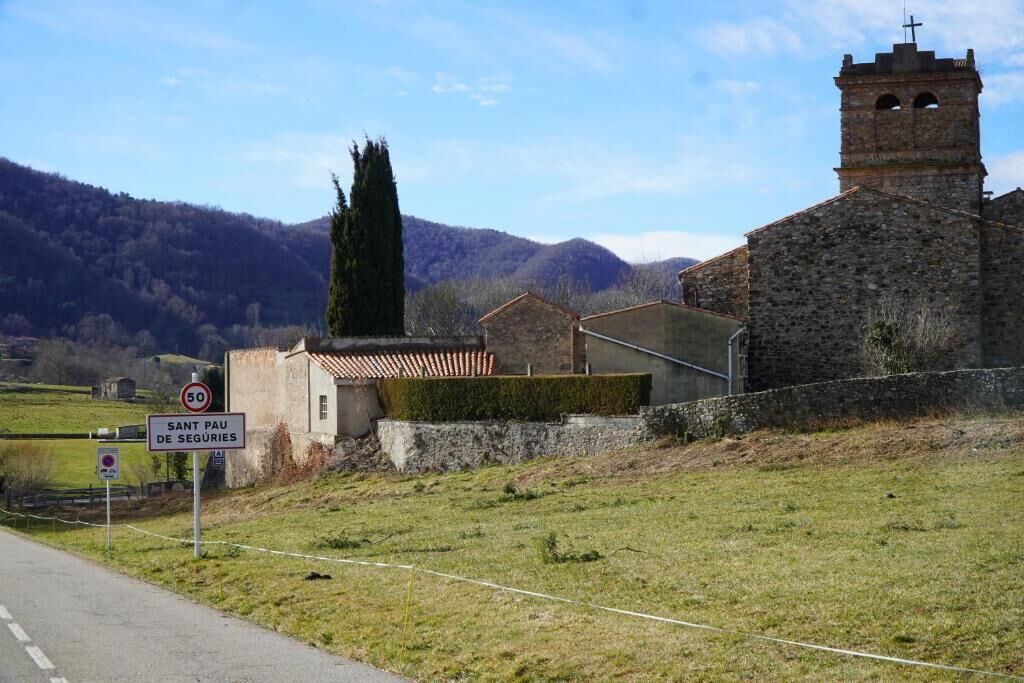 Une route de campagne avec un panneau indiquant la limitation de vitesse, une église dotée d’un clocher et un panneau signalant une zone de stationnement.