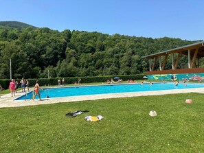 Ein Schwimmbecken, umgeben von einer Rasenfläche, mit einem bewaldeten Hügel im Hintergrund.
