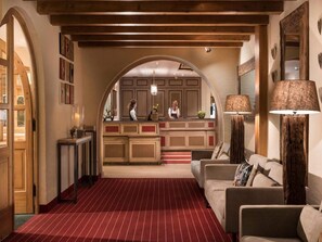 Eine Hotelhalle mit einer Rezeption, einem rot ausgelegten Bereich und einer Sitzecke.