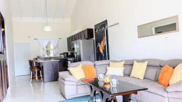 A modern living room with a grey sofa, a coffee table, and a kitchen area in the background.