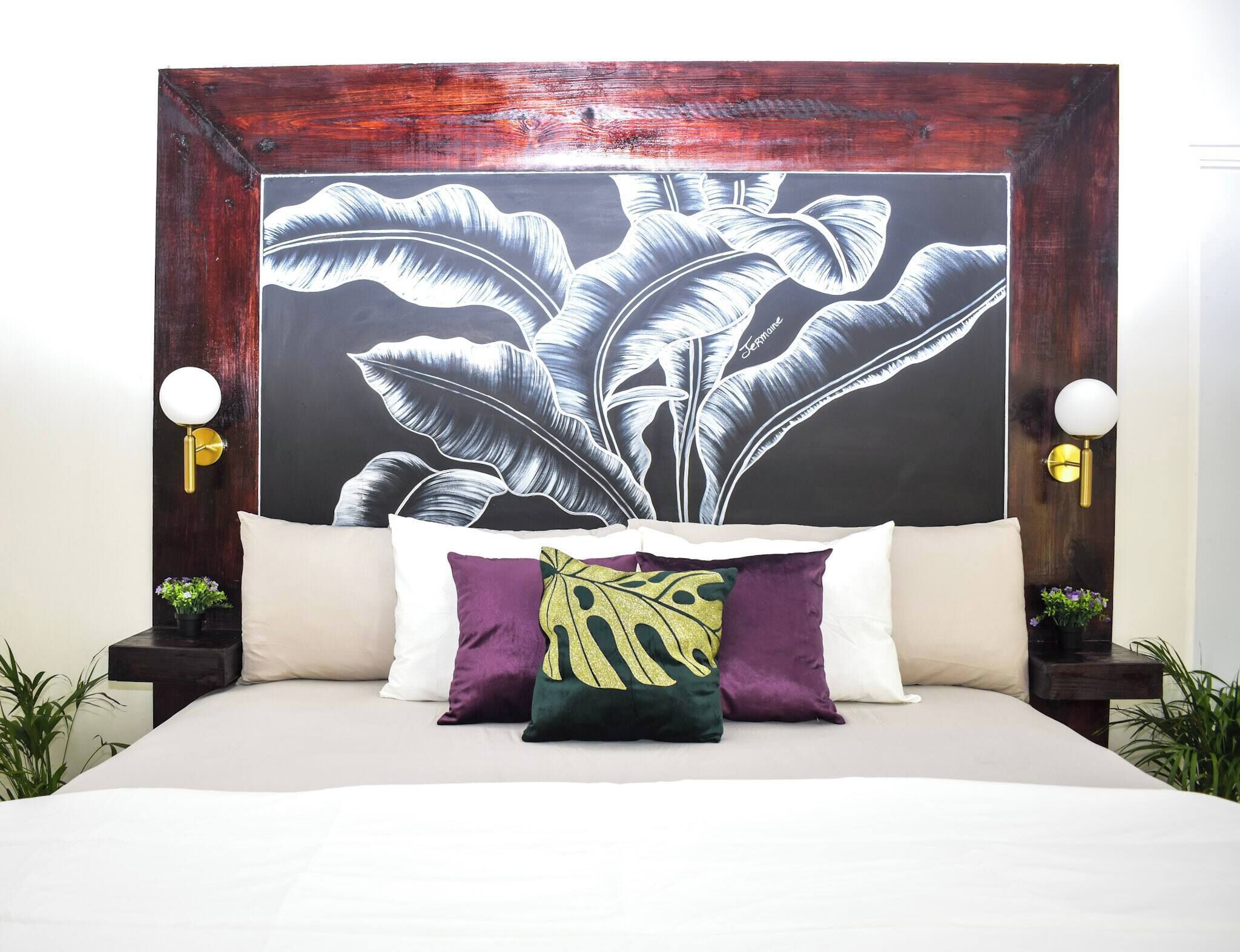 A bed with white bedding, a large botanical print headboard, and two bedside tables with wall-mounted lamps.