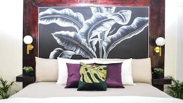 A bed with white bedding, a large botanical print headboard, and two bedside tables with wall-mounted lamps.