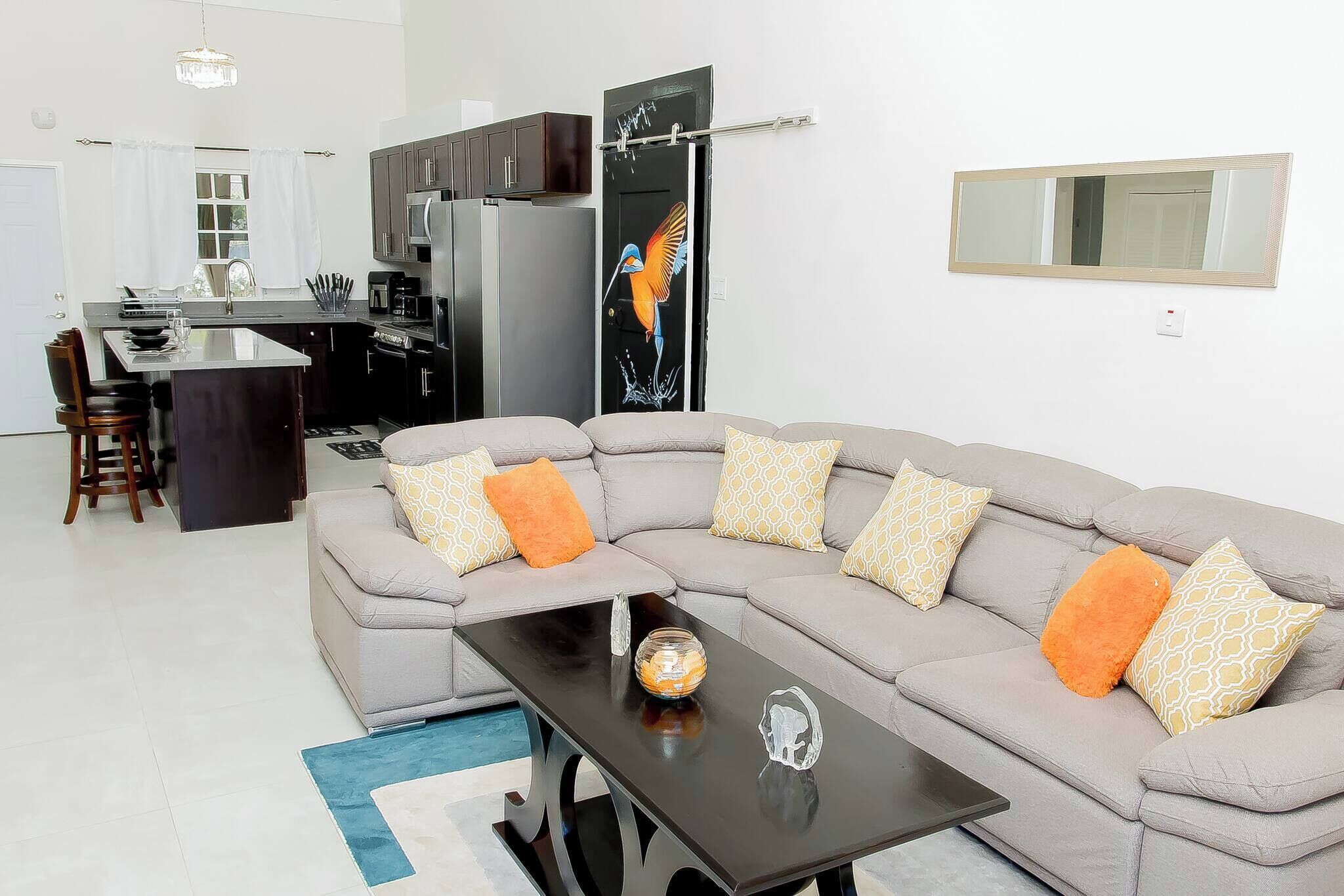 A modern living room with a grey sectional sofa, a black coffee table, and a kitchen area in the background.