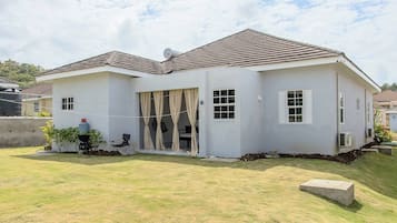 A two-story house with a flat roof, a front porch with a chair, and a small garden area.