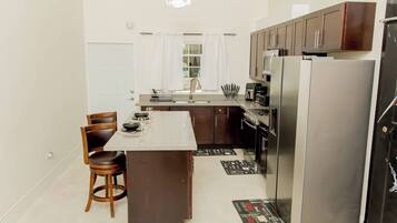 A modern kitchen with a central island, dark wooden cabinets, stainless steel appliances, and a chandelier.