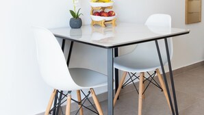Un'area pranzo moderna con un tavolo bianco, due sedie bianche e una piccola orchidea in vaso.