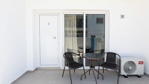 Un balcone con una porta vetrata, due sedie, un tavolino rotondo e un condizionatore d'aria bianco.