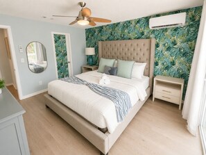 Ein Schlafzimmer mit einem Bett, einem Deckenventilator, einem Nachttisch und einer Wand-Klimaanlage.