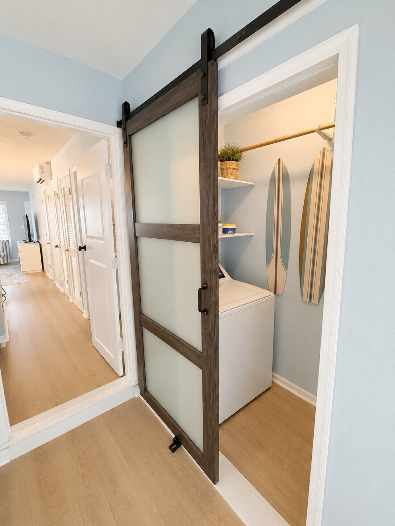 Un pasillo con una puerta corredera que da a un área de lavandería con lavadora y estantes.