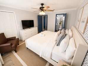 A bedroom with a bed, a TV, a ceiling fan, a dresser, and a chair. - Fully Renovated Beach Retreat Townhome! (Panama City Beach)