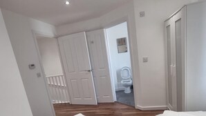 A bedroom with two beds, a wardrobe, and a bathroom visible through an open door.