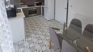 A compact kitchen with modern appliances, a dining area with a table and chairs, and patterned floor tiles.