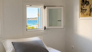 A bedroom with a bed, a window with a view of the sea, and a wall-mounted artwork.