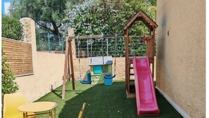 Ein Spielbereich für Kinder mit Rutsche, Schaukeln und Kunstrasen.