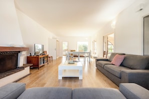 A modern living room with a fireplace, a sofa, a coffee table, and a dining area. - Cabanas Jardim da Ria: a private home with a large garden, a pool, and views of the estuary (Tavira)