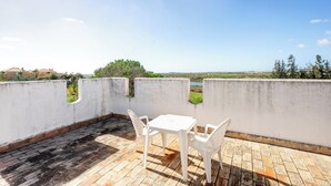A terrace with a white table and chairs, a brick floor, and a view of a distant landscape. - Cabanas Jardim da Ria: a private home with a large garden, a pool, and views of the estuary (Tavira)