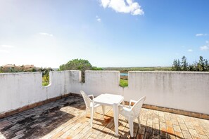 A terrace with a white table and chairs, a brick floor, and a view of a distant landscape. - Vrbo Property (Tavira)