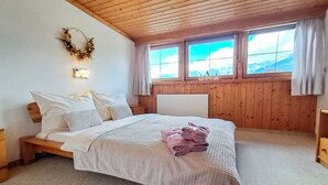 A bedroom with a wooden ceiling, a bed with white bedding, a view of mountains through windows, and a wreath on the wall. - Pessenteiner by Interhome (Saalfelden am Steinernen Meer)