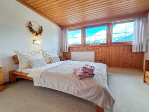 A bedroom with a wooden ceiling, a bed with white bedding, a view of mountains through windows, and a wreath on the wall. - Pessenteiner by Interhome (Saalfelden am Steinernen Meer)