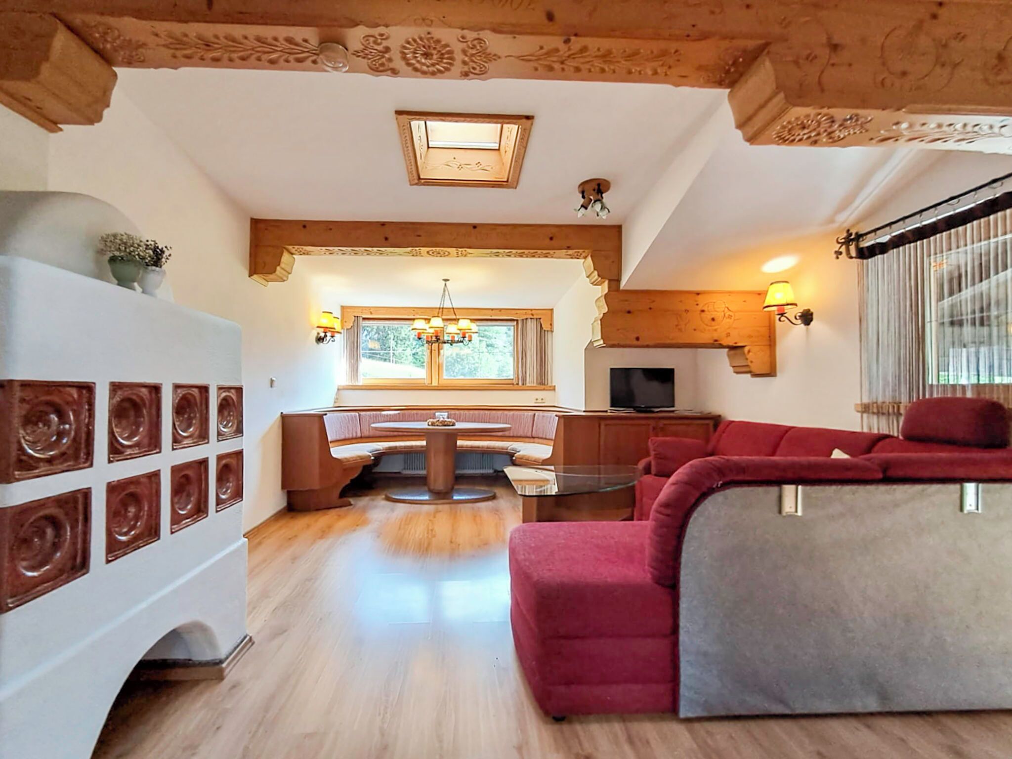 Una sala de estar acogedora con un sofá rojo, un comedor con banco, un televisor y un techo de vigas de madera.