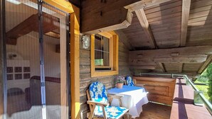 A wooden cabin with a balcony, a table with a white tablecloth, a chair with a floral cushion, and a window with a wooden frame. - Pessenteiner by Interhome (Saalfelden am Steinernen Meer)
