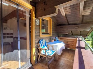 A wooden cabin with a balcony, a table with a white tablecloth, a chair with a floral cushion, and a window with a wooden frame. - Pessenteiner by Interhome (Saalfelden am Steinernen Meer)