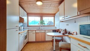 A compact kitchen with wooden cabinets, a built-in oven, a dining table with chairs, and a window with a view of trees. - Pessenteiner by Interhome (Saalfelden am Steinernen Meer)