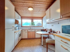 A compact kitchen with wooden cabinets, a built-in oven, a dining table with chairs, and a window with a view of trees. - Pessenteiner by Interhome (Saalfelden am Steinernen Meer)