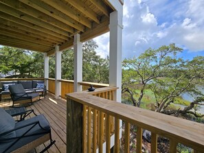 A covered outdoor deck with a wooden railing, a sofa, and chairs. - 4bedroom house in fantastic Gulf Shores with long pier for fishing and gathering (Gulf Shores)