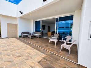 Et overdækket udendørsområde med terrasse, siddepladser og udsigt til himlen.