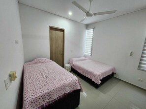 A bedroom with two single beds, a ceiling fan, a door, and a window with blinds.