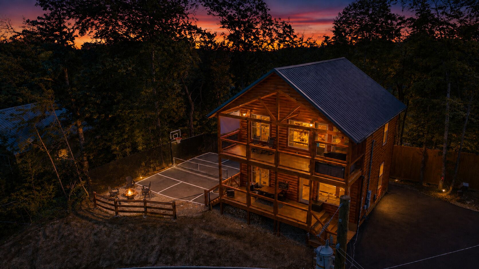 Warmly lit cabin retreat with private sport court and fire pit at sunset
