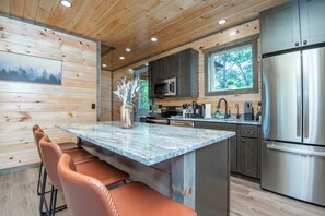 A modern kitchen with a central island, stainless steel appliances, and wooden paneling. - Pigeon Forge Sunsets- Cabin With Mountain Views (Sevierville)