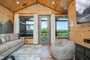 A cozy cabin interior with a wooden ceiling, a sofa, a bean bag, a large window, and a door leading outside. - Pigeon Forge Sunsets- Cabin With Mountain Views (Sevierville)