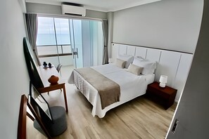 Una habitación de hotel moderna con una cama grande, mesitas de noche, un escritorio con silla y un amplio ventanal con cortinas.