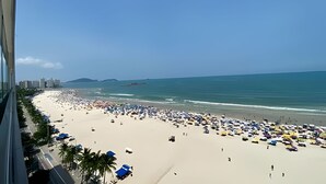 Una playa con numerosos paraguas, gente, cielo despejado y edificios al fondo.
