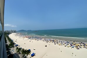 Una playa con numerosos paraguas, gente, cielo despejado y edificios al fondo.