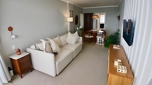 Una sala de estar con un sofá, una mesita de madera, una lámpara y un comedor con mesa y sillas.