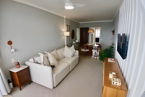 Uma sala de estar com sofá, mesa lateral de madeira, luminária e área de jantar com mesa e cadeiras.