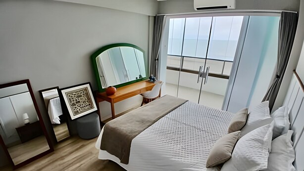 A bedroom with a large bed, a wooden dresser, a mirror, and a view of the balcony. - SHB - Alto Padrão com Vista  (Guarujá)