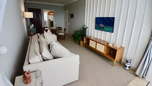 A living room with a sofa, a TV, a wooden cabinet, and a dining area in the background. - SHB - Alto Padrão com Vista  (Guarujá)