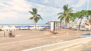 A beachside promenade with palm trees, a bus stop, and beach umbrellas. - SHB - Alto Padrão com Vista  (Guarujá)